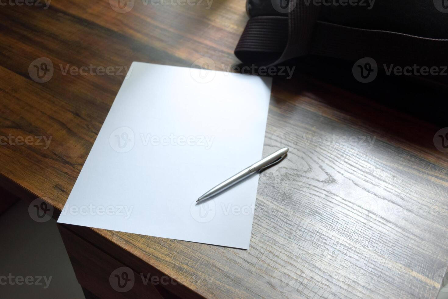Pen and blank paper and work bag placed on a wooden patterned work desk in soft sunlight background for concept of office and take note. photo