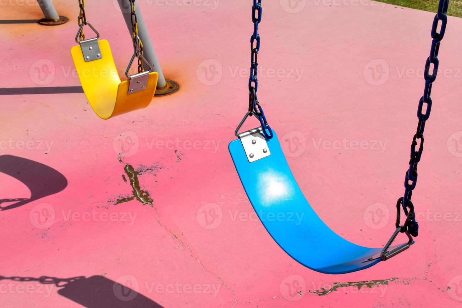 Blue and yellow swings with black chain on broken red concrete floor background at outdoor playground. photo