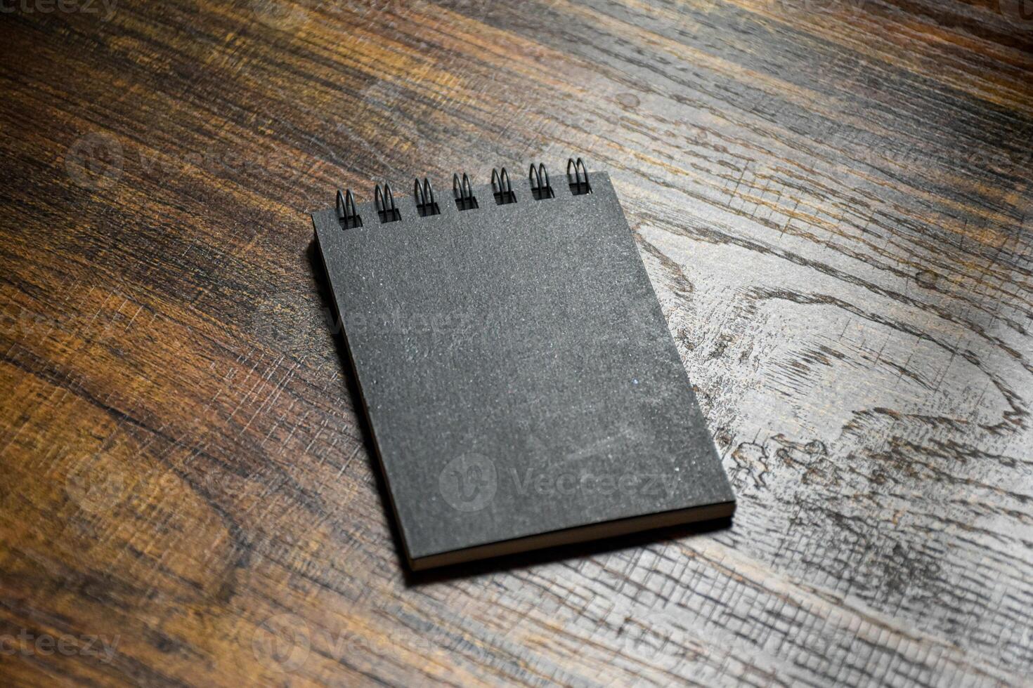 Small black notebook sits on a wooden patterned desk for taking notes or writing. photo
