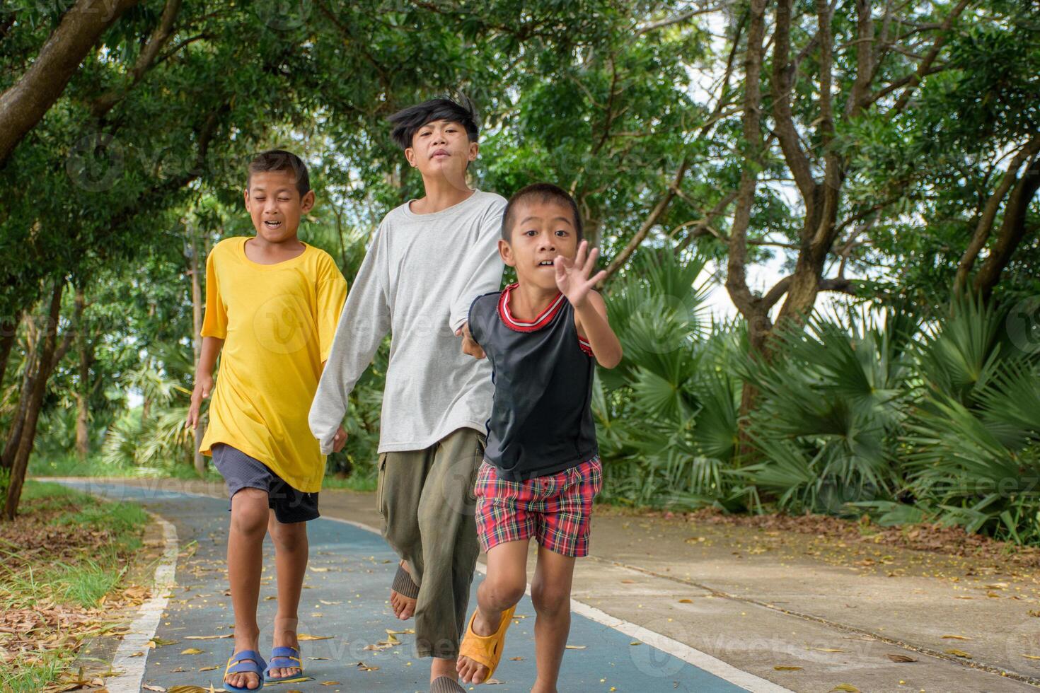 Group of three Asian boys were running fast without care is causing an accident or falling in danger on the road in the park on forest background. photo