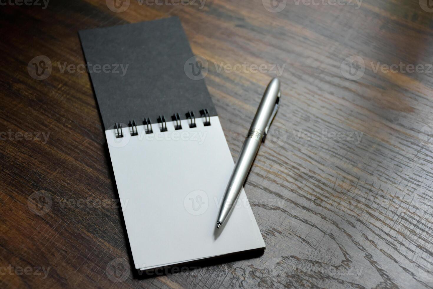 Silver pen and blank paper of notebook placed on wooden pattern desk at office for design ideas and taking notes. photo