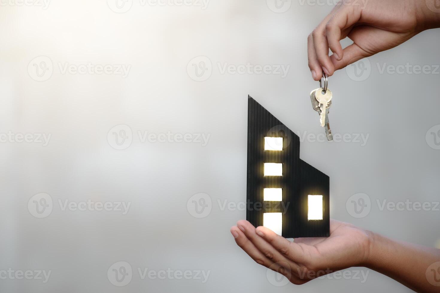 Business man hand holding miniature commercial building model and keys on blurred concrete background for real estate and building construction concept. photo
