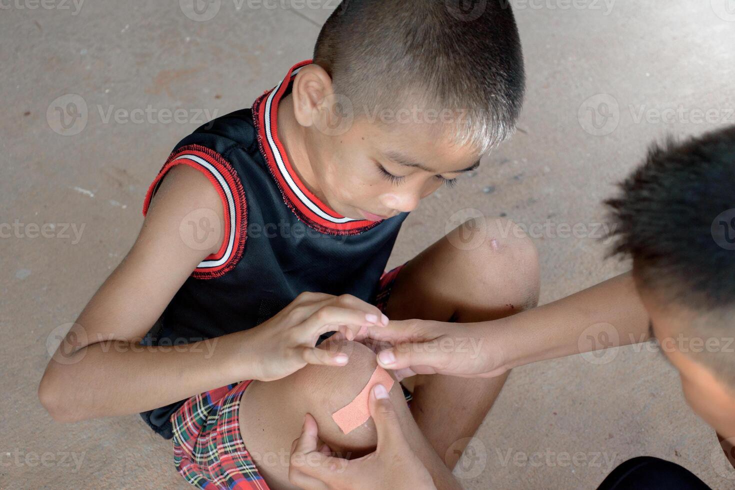 Two little boys help bandage an injured boy's wound For children's first aid and accident concepts is top view. photo