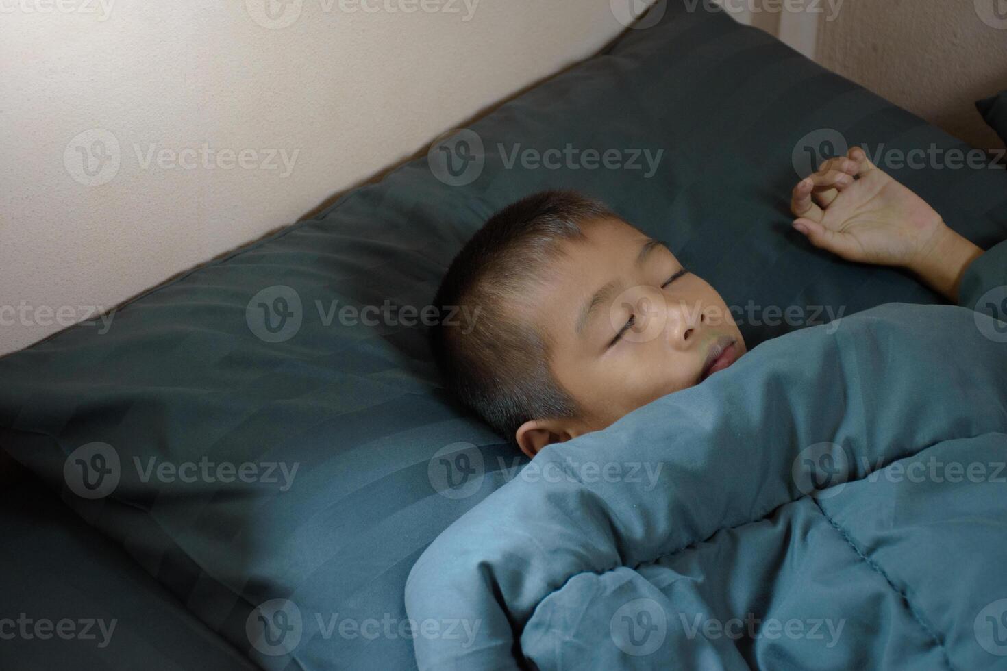 Asian young boy who is lying on the bed and has not yet woken up in the morning and wakes up late in the bedroom with the morning sun in the background. photo