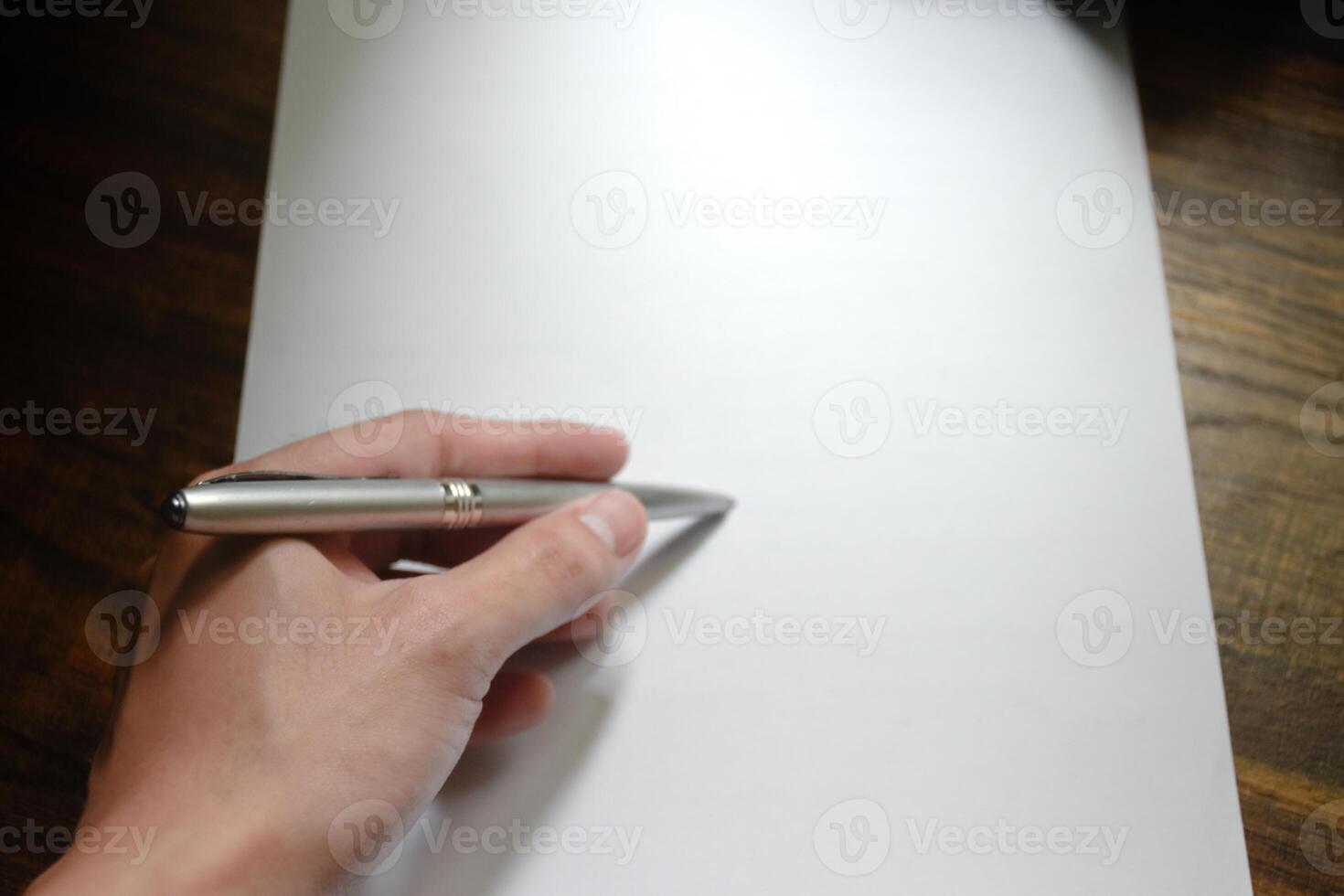 Hand writing with pen over blank paper on wooden work desk beautiful pattern,concept of idea and actions,Hand holding for pen,Work equipment in workplace,Hand close-up with pen and paper. photo