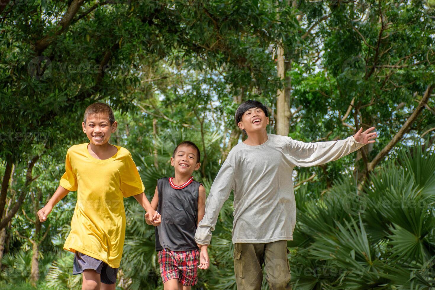 Group of children are holding hands and running joyful and happily at the park in green forest background for lifestyle and outdoor activities. photo