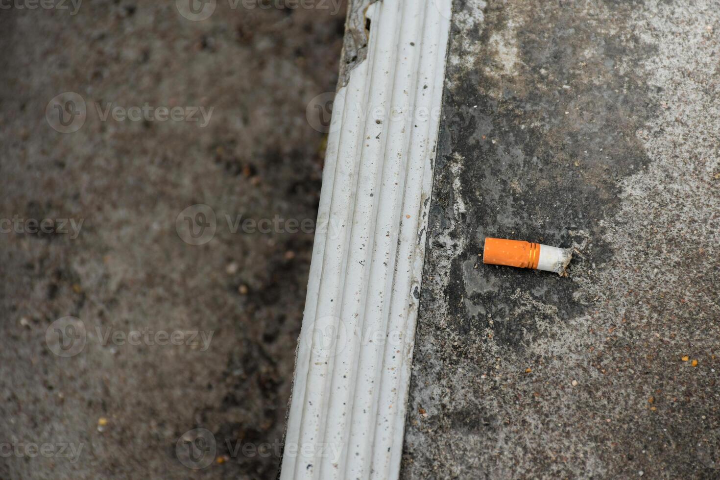 Smoked cigarette butts that are improperly discarded on public concrete steps are an environmental and health hazard in a dark tone background. photo
