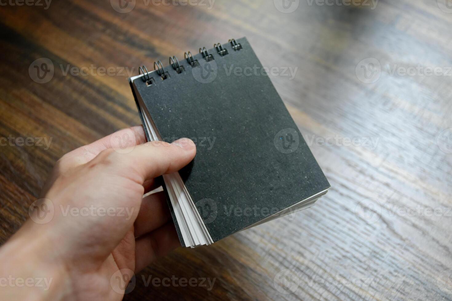Business man hand holding a small black notebook on desk table wooden pattern at office. photo