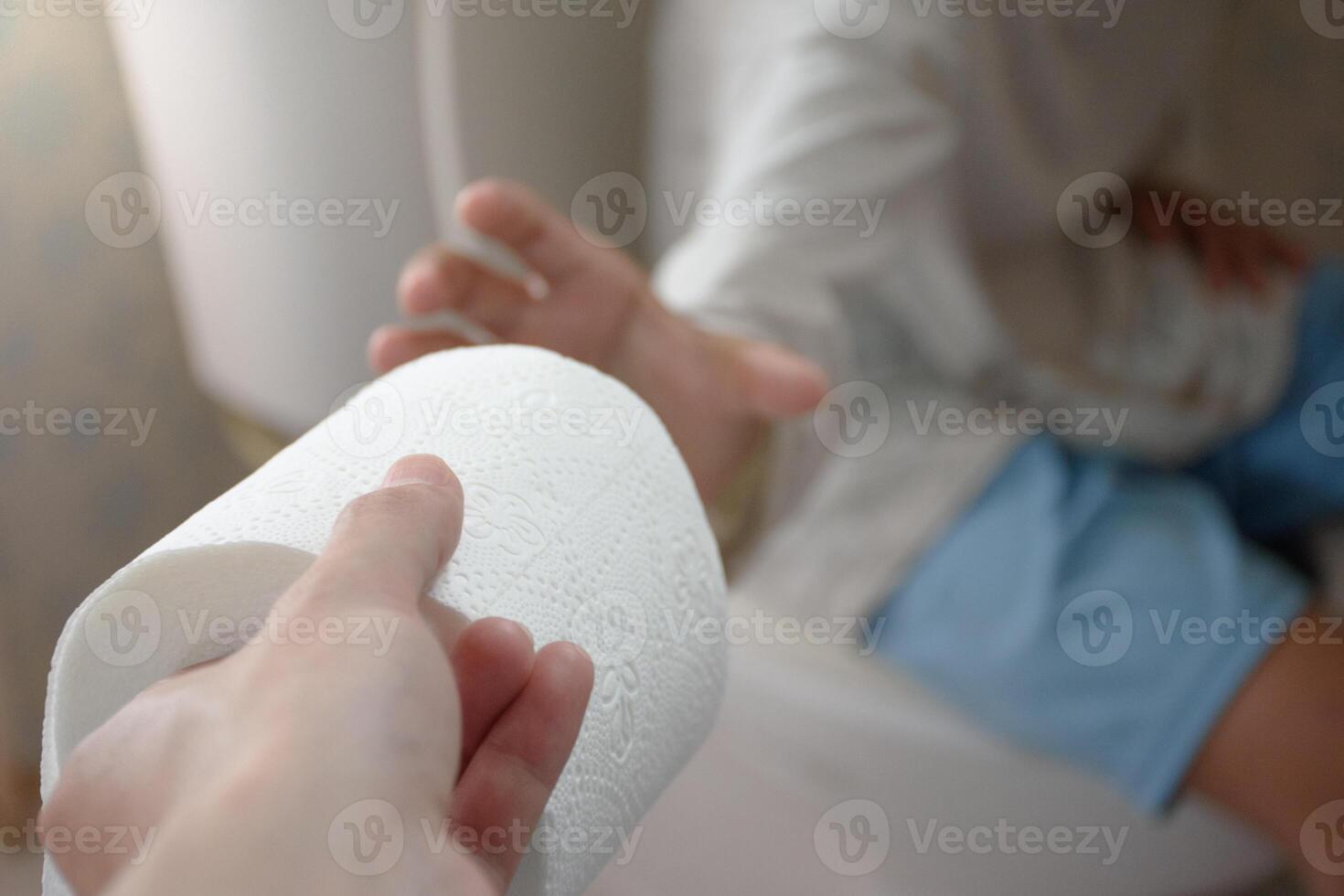 Close-up hand holding a toilet roll or tissue handed it to a man sitting on the toilet bowl in bathroom and sunlight blurred background concept of excretion and hygiene. photo