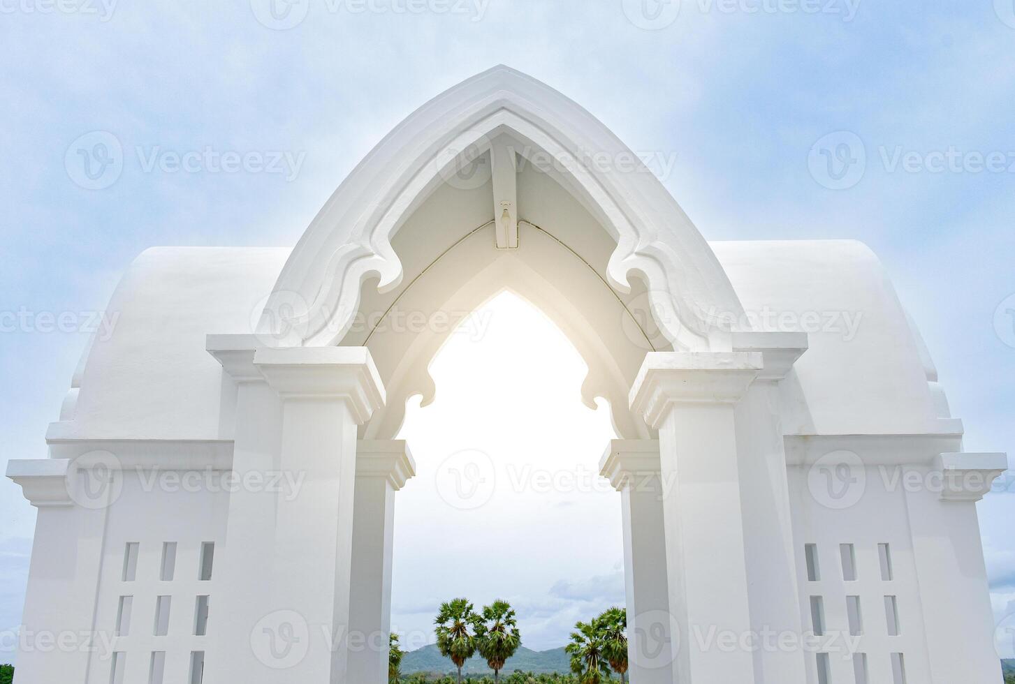 Beautiful white entrance arch architecture with Thai temple pattern with Indian pattern or a white Thai temple chapel with sunlight in the center on sky and forest background. photo