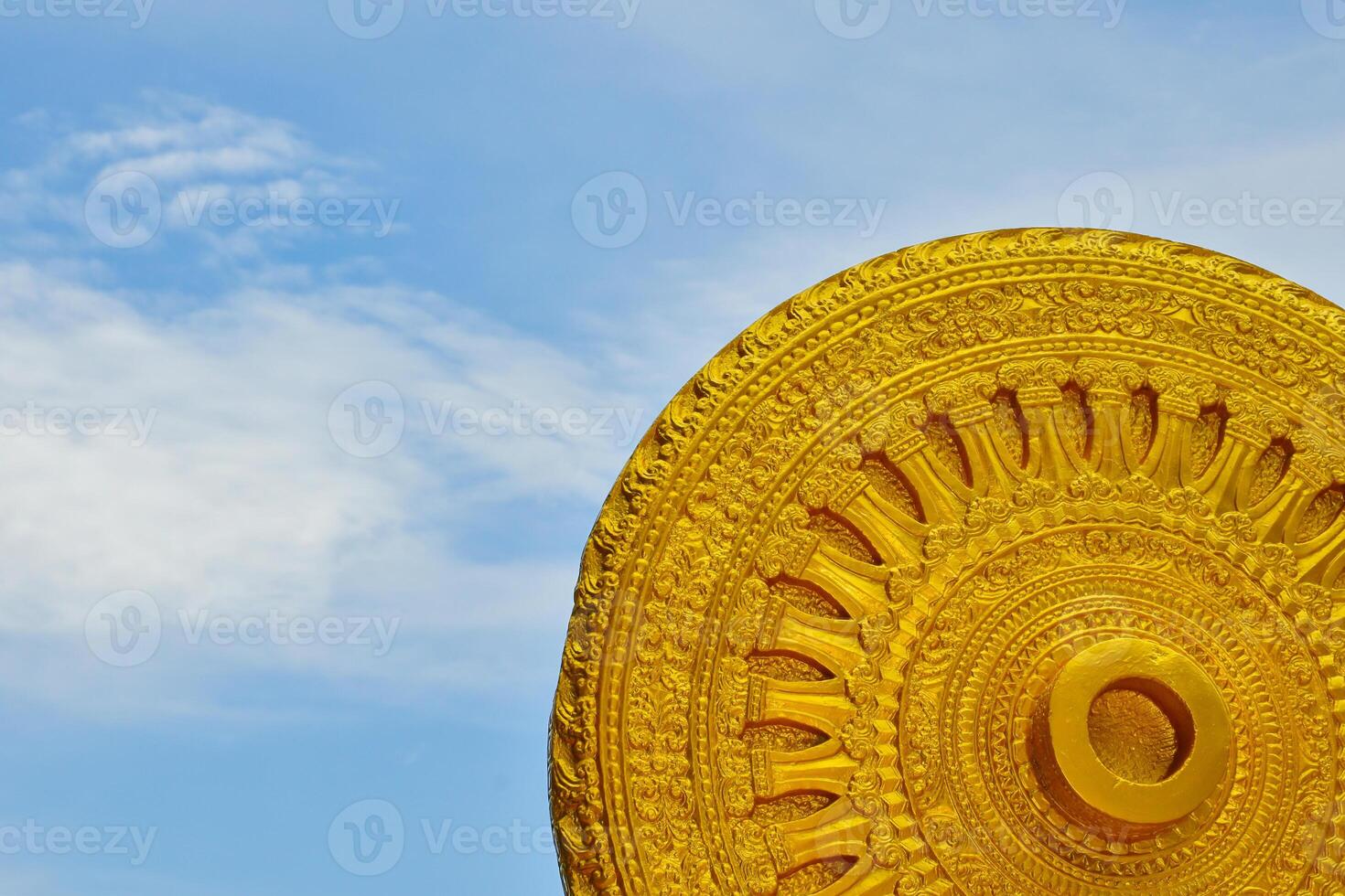 The Wheel of Life and Buddhist Stories is a golden yellow sculpture with Asian Buddhist motifs against a beautiful blue sky background. photo