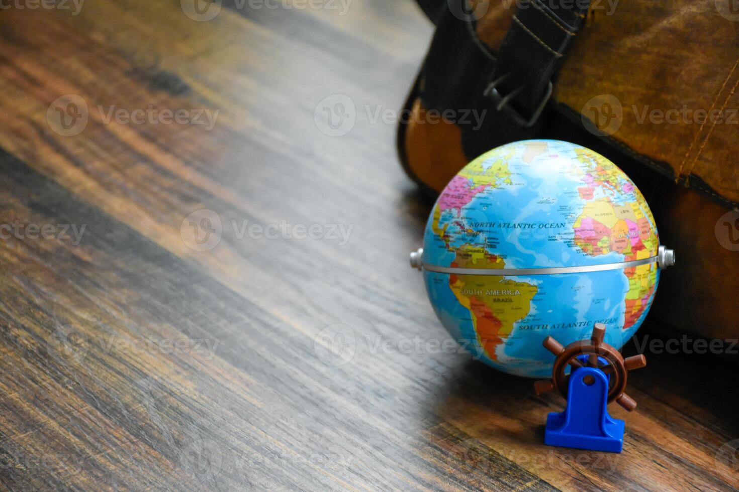 Globe showing maps of America and Africa with miniature ship steering wheel model for world travel and maritime business concepts on the wooden pattern table. photo
