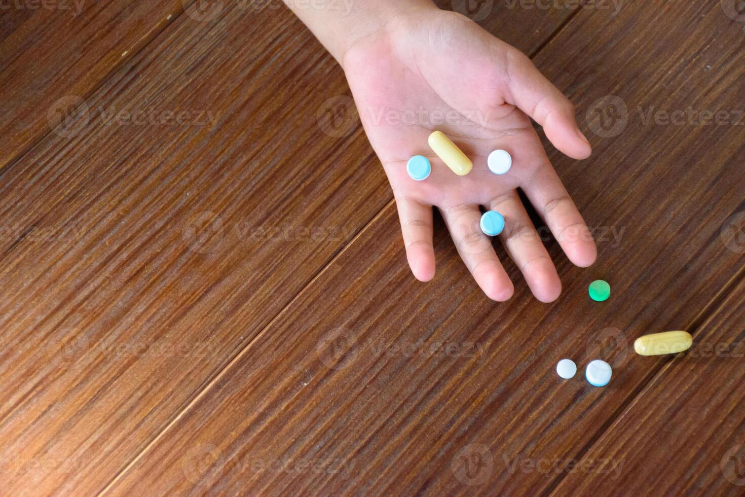 Many pills on hand and on wood pattern floor top-view different colored tablets and capsules indicate an overdose for concept of medicine and medical. photo