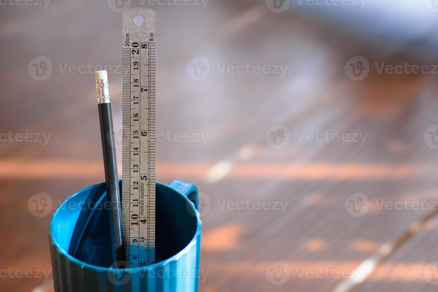 Close up of pencil and ruler in blue plastic cup as school supplies or sketching and design on blurred brown wooden background. photo