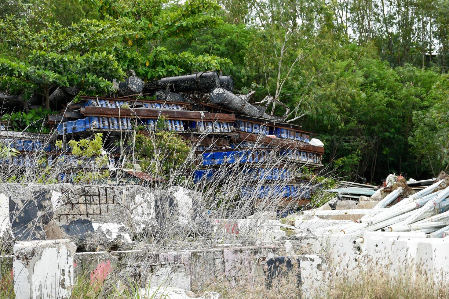 Old storage place or junkyard there are old and crumbling concrete road barrier and many broken and rusted industrial steel structures in desolate forest background. photo
