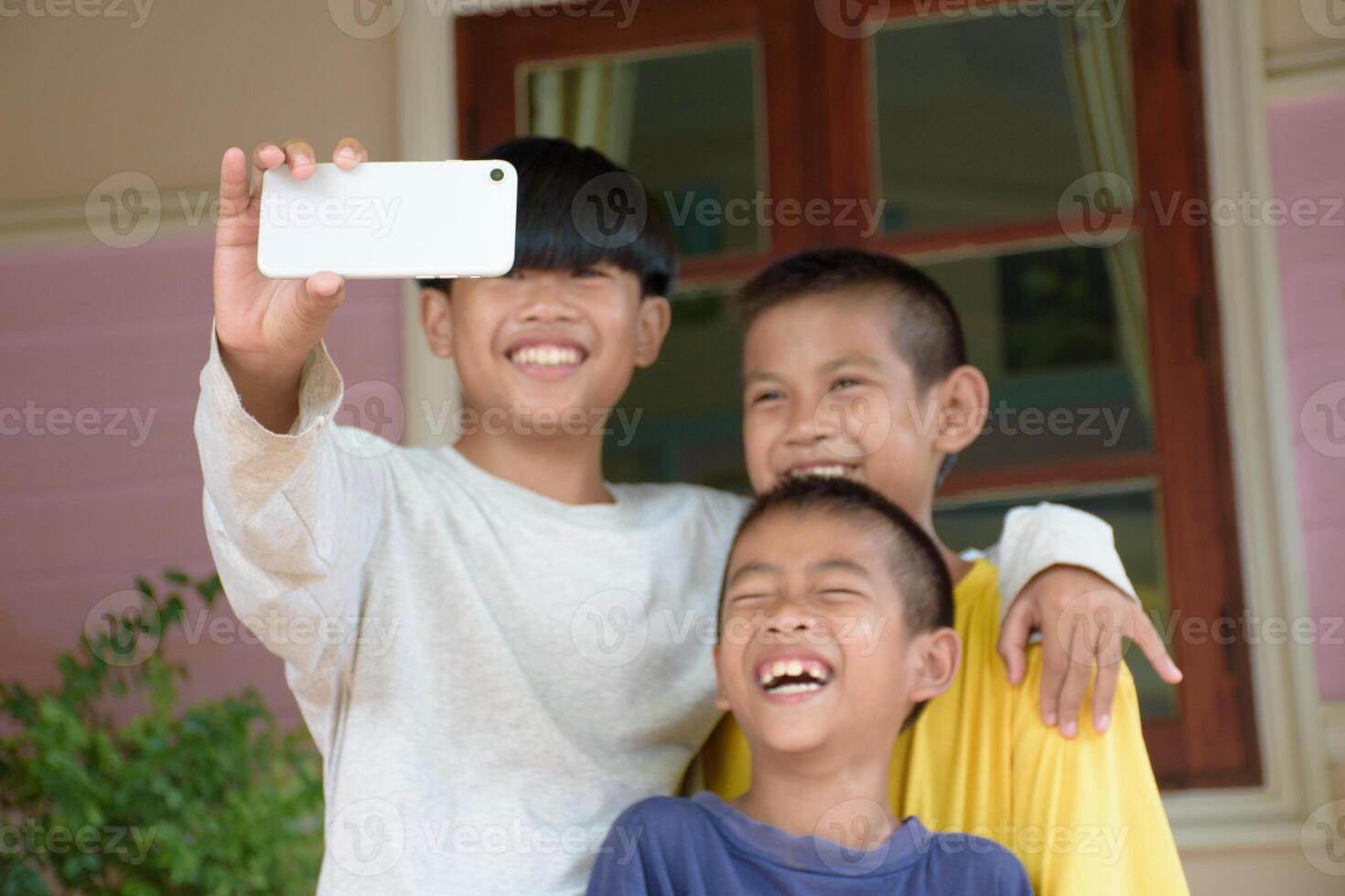 Close up of smartphone and a group of Asian boys taking group selfies against the background of outdoors and a green forest. Three boys smiling charmingly and taking pictures using smartphones. photo