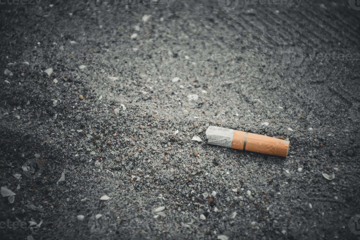 Cigarette butts on the sand with shell fragments on the beach have a negative effect on the marine environment in dark black tone background. photo