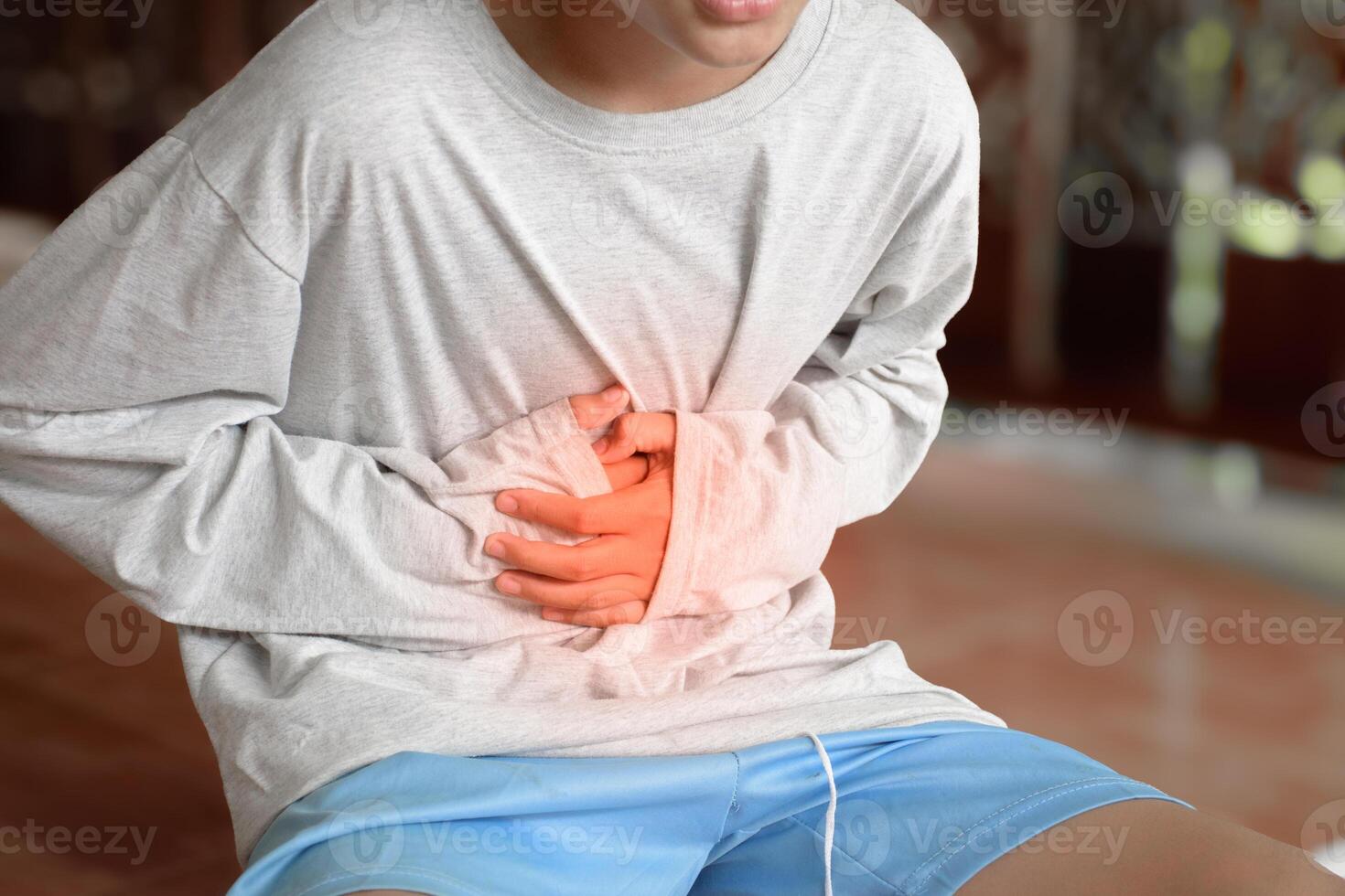 Young man in a gray shirt was holding his stomach with both hands due to stomach pain. The boy had a stomach ache and touched his stomach with a hand with red spots on the blurred background. photo