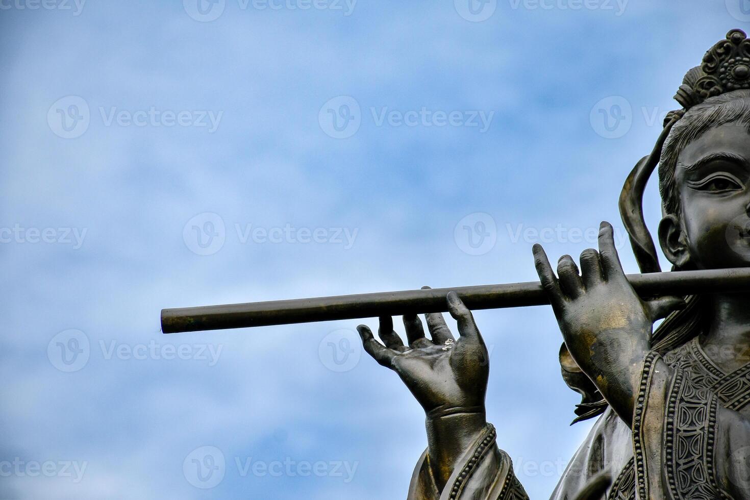 Sculpture of a black iron Chinese god playing a flute, a god in Chinese literature and revered on a blue sky background photo