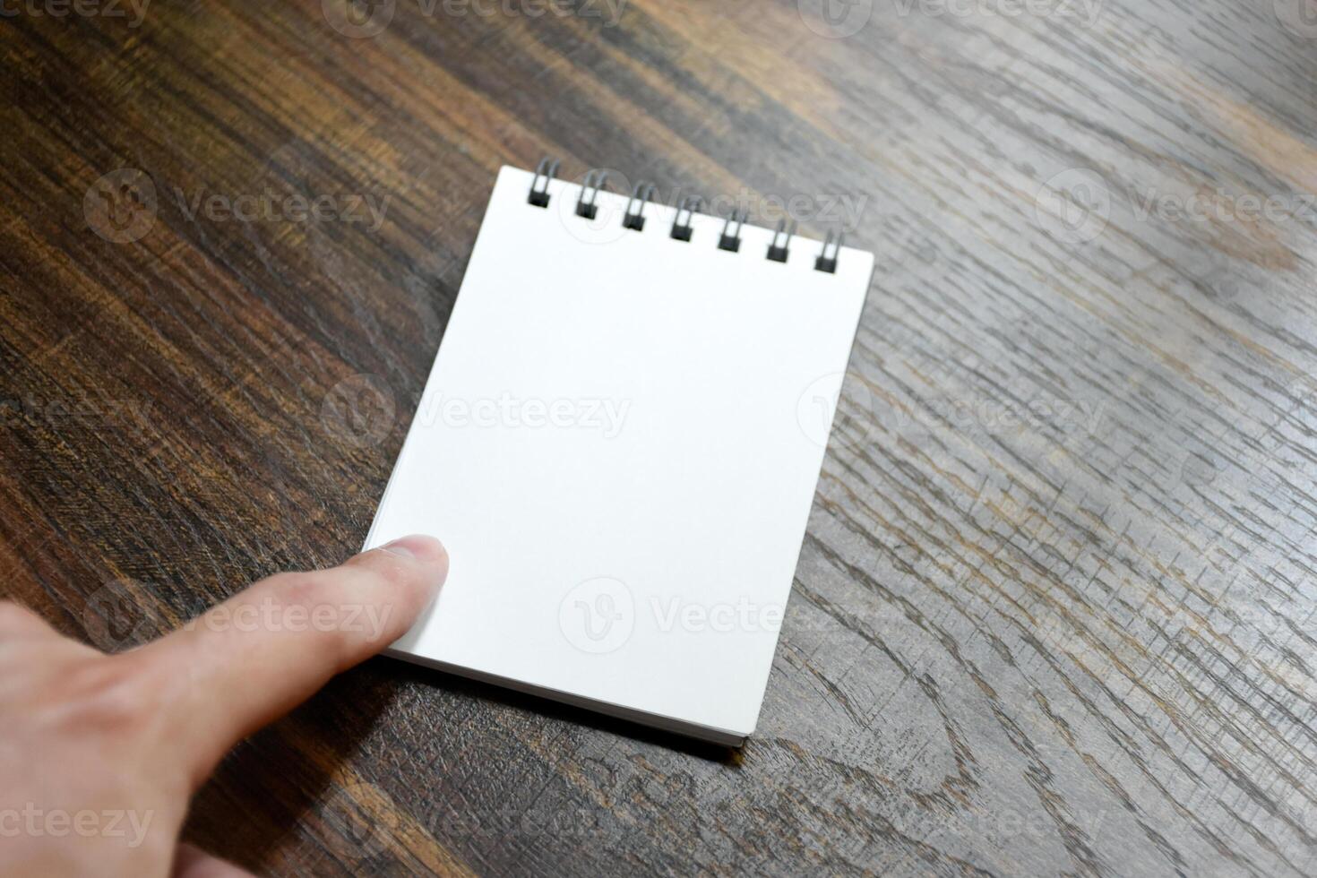 Hand pointing at blank white paper of notebook on wooden patterned desk background at office. photo