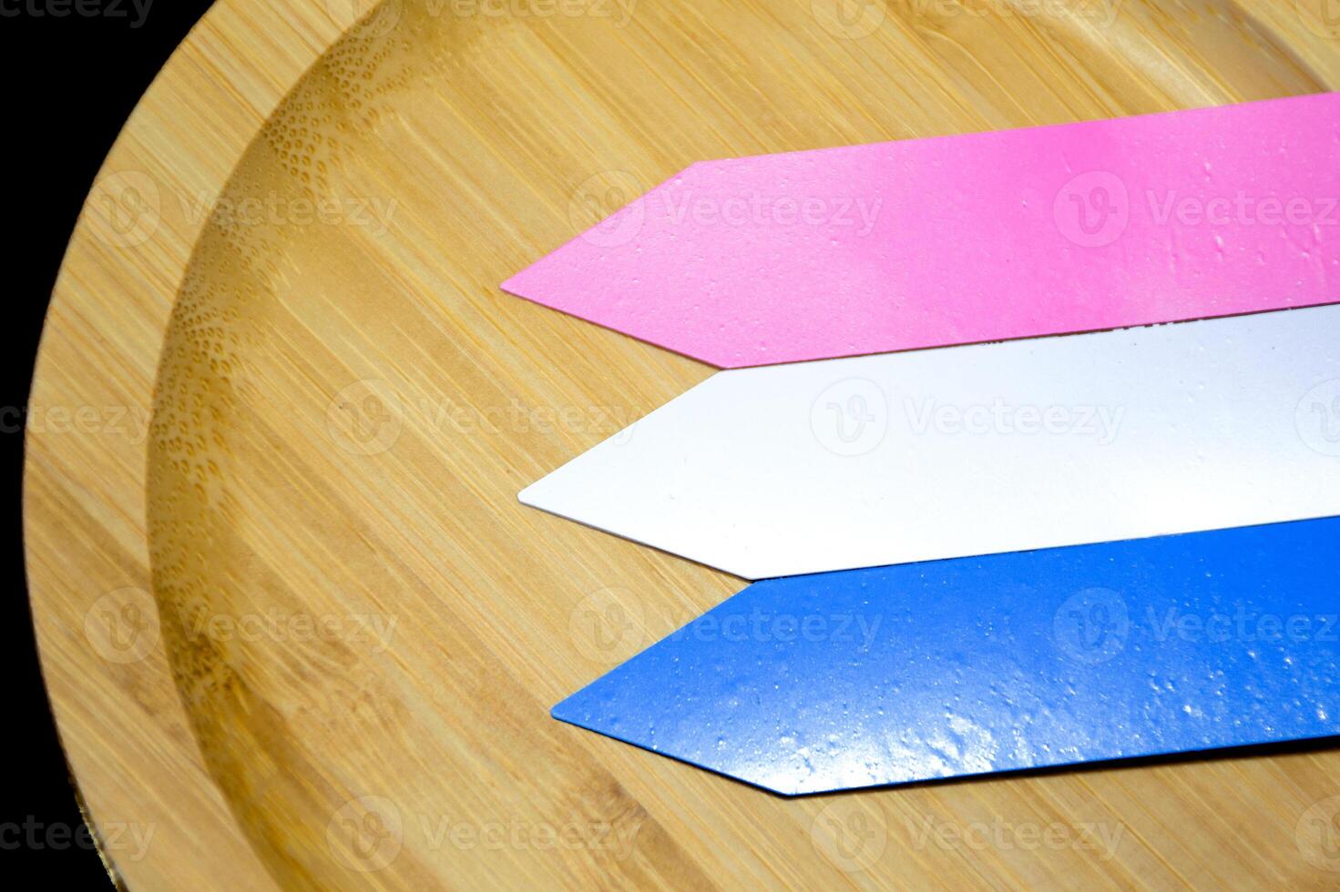 Close-up three plastic name tags in blue, white and pink for plant names or to add text are placed on beautifully patterned wooden plates over a black background. photo