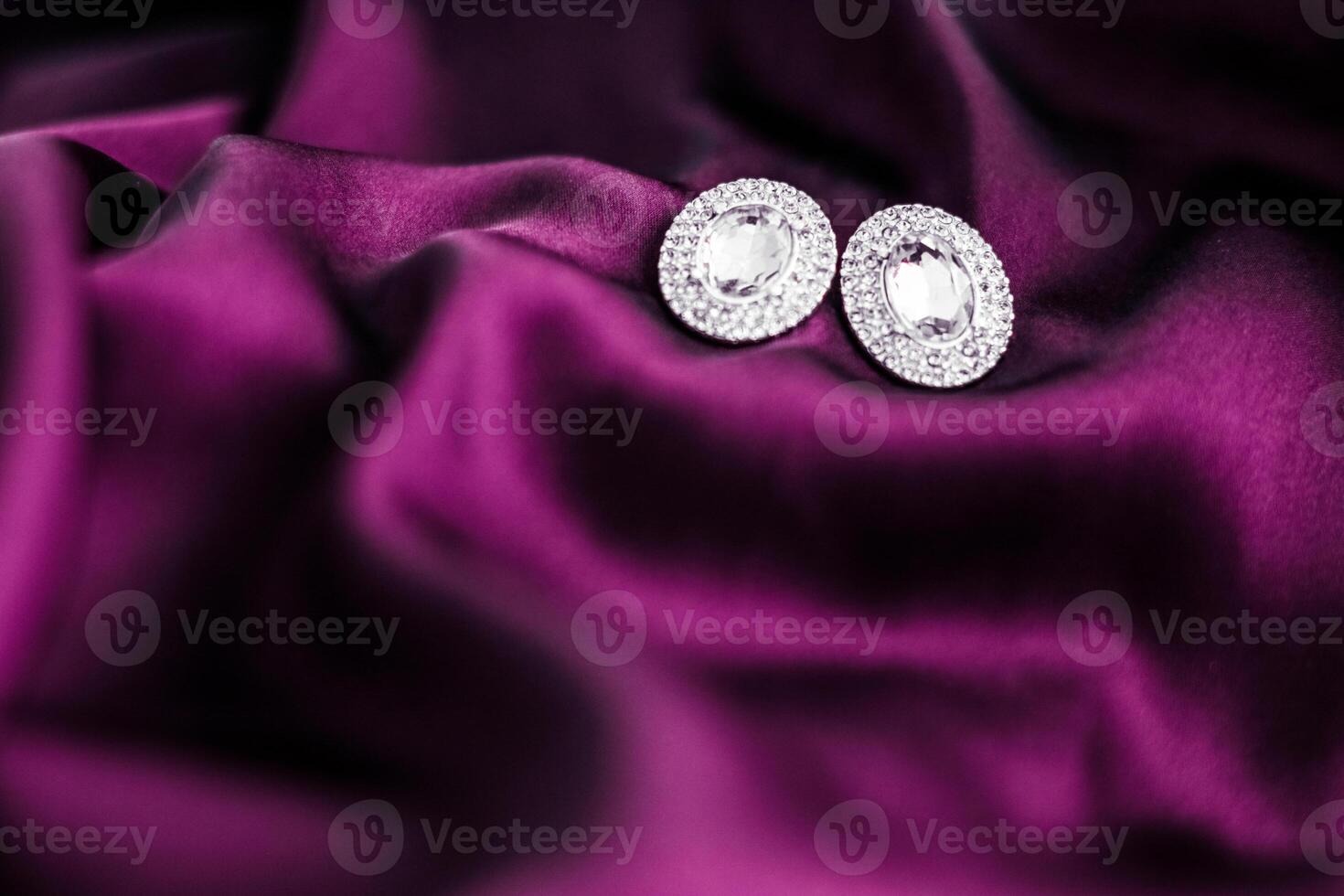 Luxury diamond earrings on dark pink silk fabric, holiday glamour jewelery present photo
