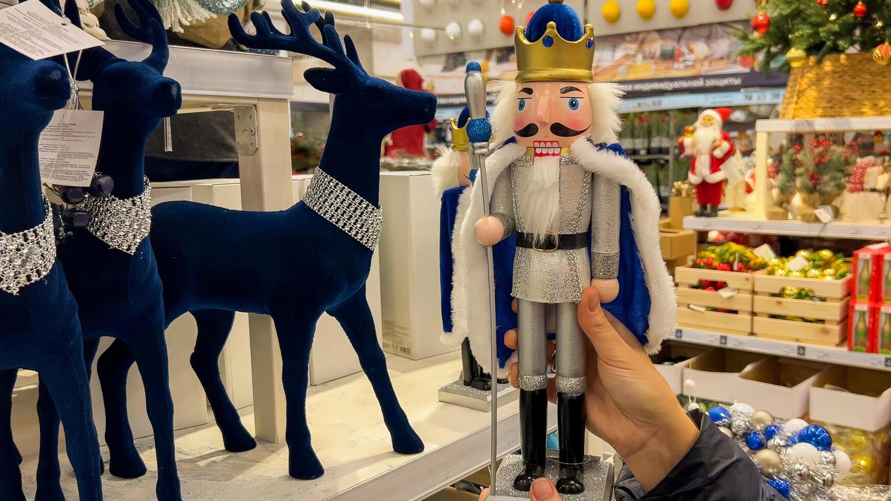 Hand holding traditional nutcracker figurine in a Christmas holiday shop with festive decorations and reindeer models, suggesting holiday shopping and seasonal decor 15 dec 2023, Shanghai, China photo