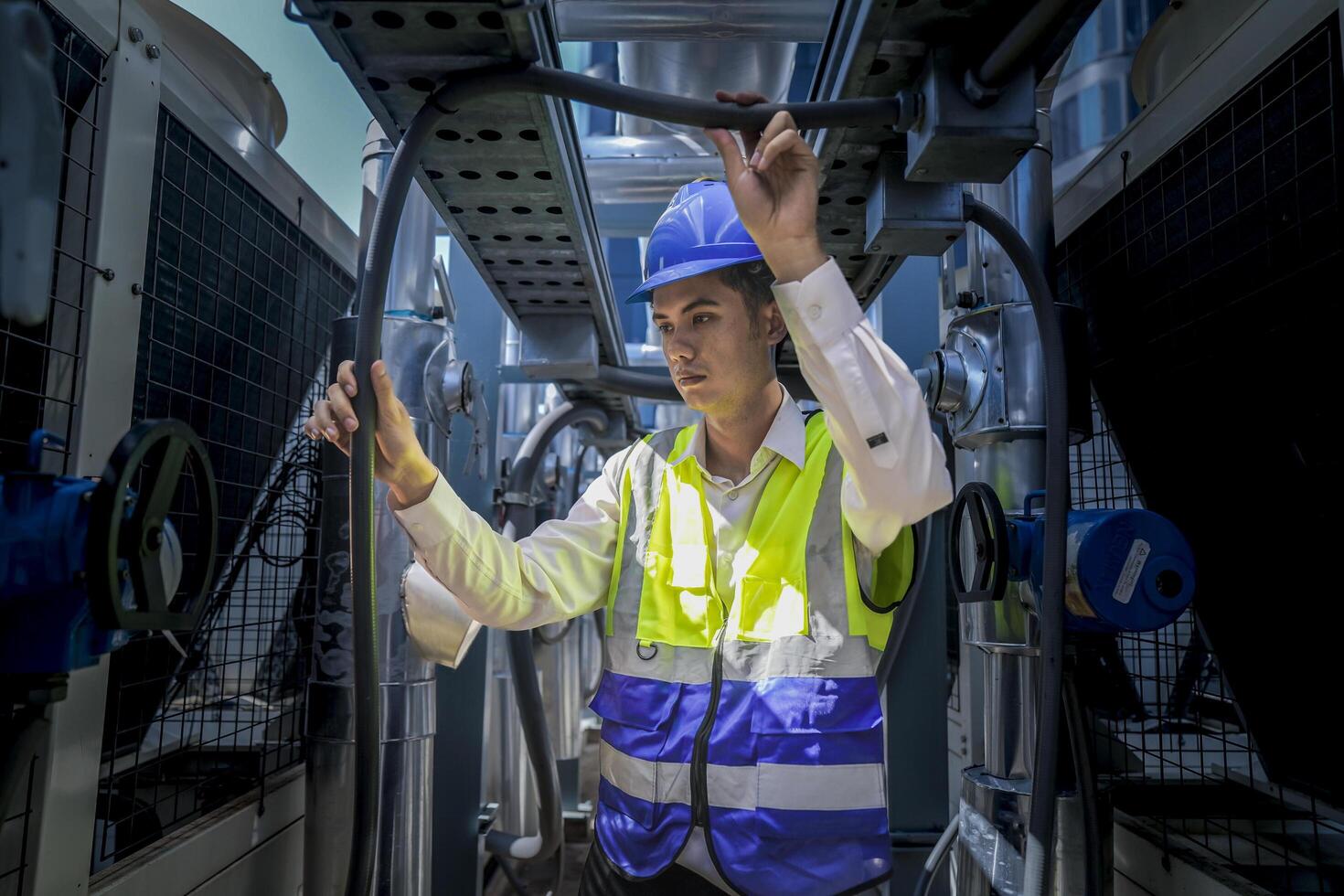 An industrial worker in high-visibility gear and a blue helmet meticulously examines the intricate network of machinery. The engineer is dedicated to maintaining operational efficiency and safety. photo
