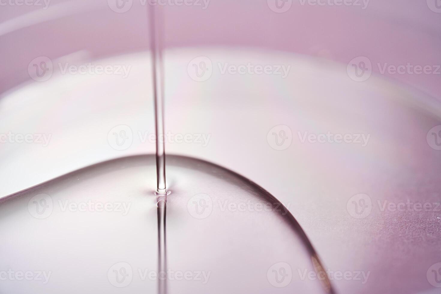 Serum or cosmetic oil flows into a transparent bowl on a purple background. photo