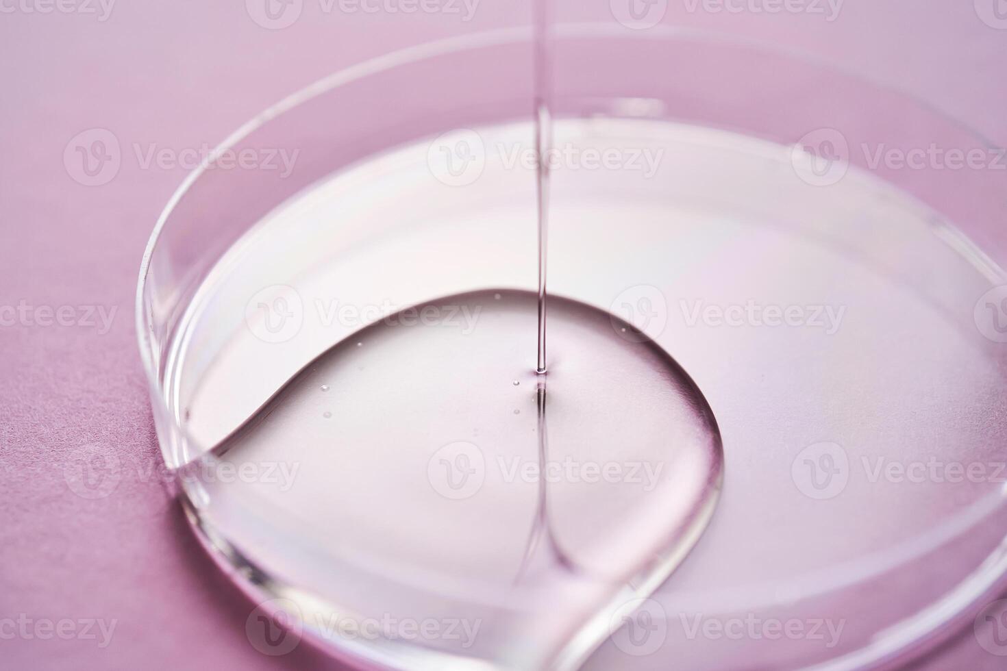 Serum or cosmetic oil flows into a transparent bowl on a purple background. photo