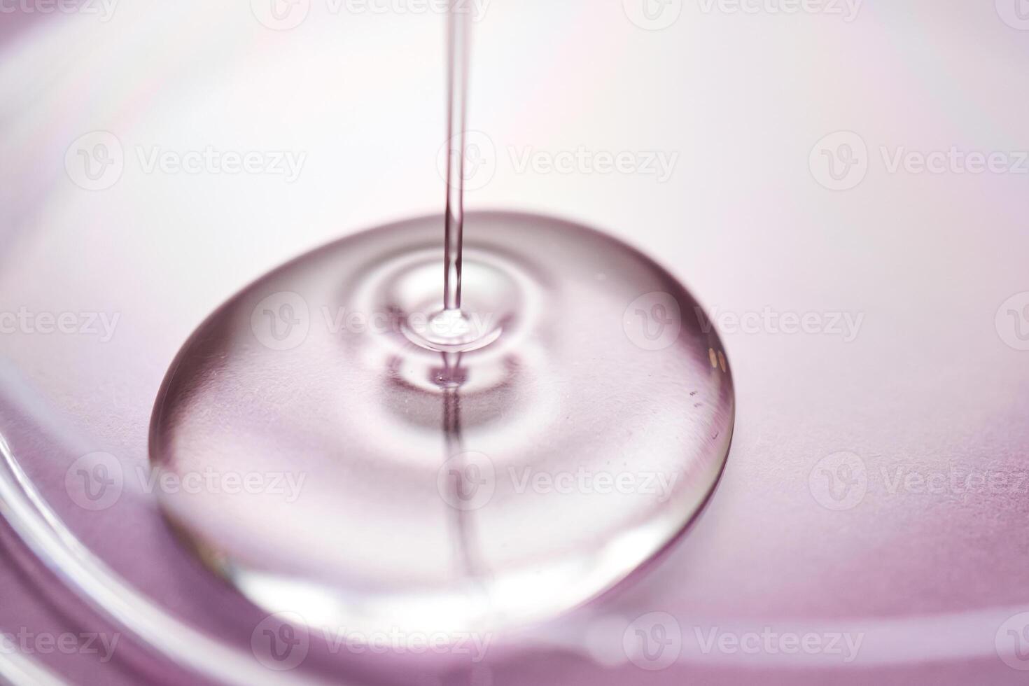 Serum or cosmetic oil flows into a transparent bowl on a purple background. photo