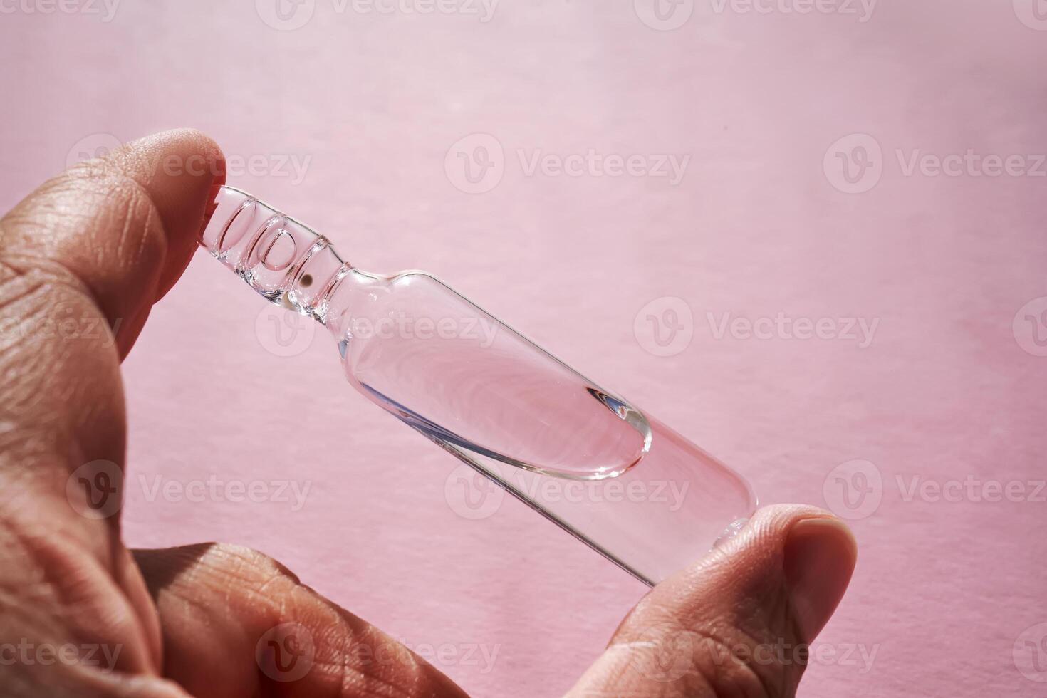 Ampoule for injection with medicines on a pink background in hand. photo