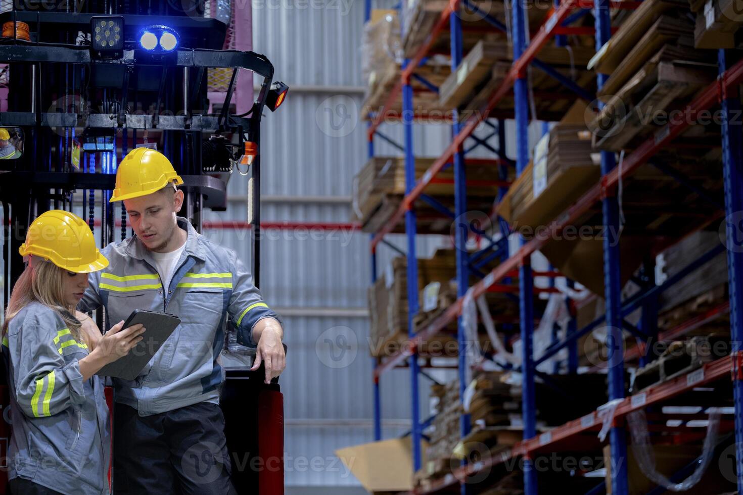 Two male and female factory checkers are discussing work on a warehouse truck. While working in a warehouse for industrial products photo