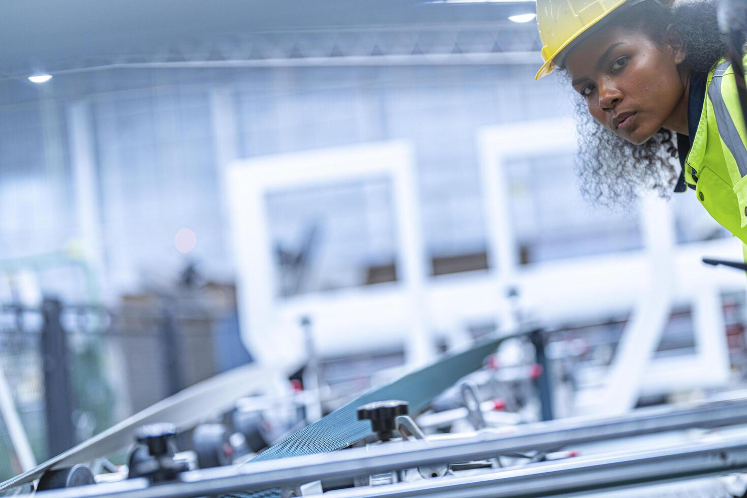 Portrait of African woman worker beautiful face with eye confident and wearing working suite dress and safety helmet at heavy machine in industry factory. Engineer worker concentrate on workplace. photo