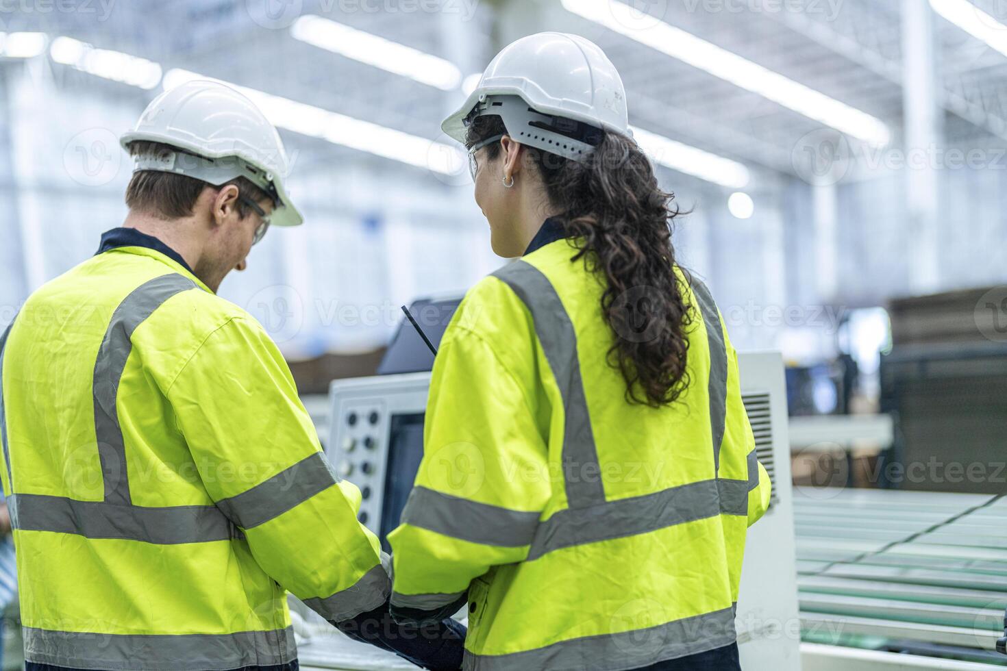 Male and female engineers in neat work clothes prepare and control the production system of large modern machines in a factory producing industrial technology products. photo