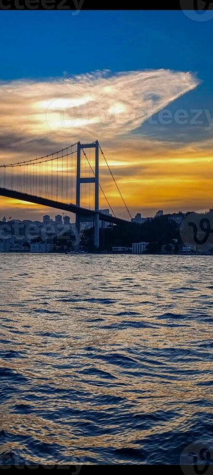 a bogazici bridge is seen from the water with the sun setting behind it.Bosphorus, Istanbul, Turkey photo