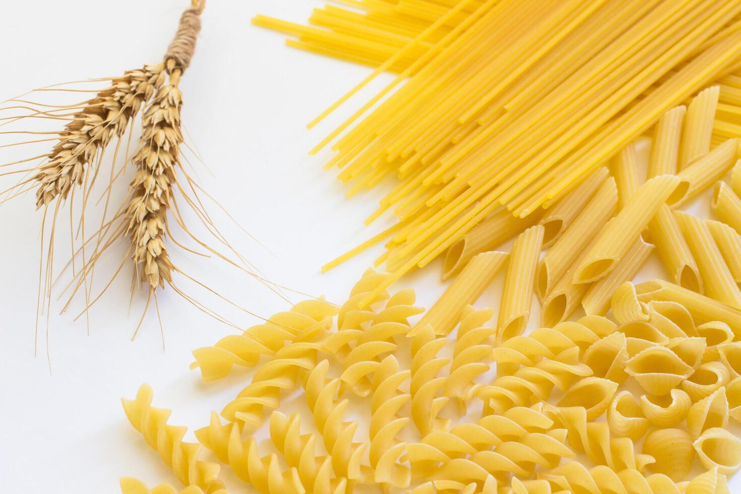 Spikelets of wheat and several types of pasta on a white background photo