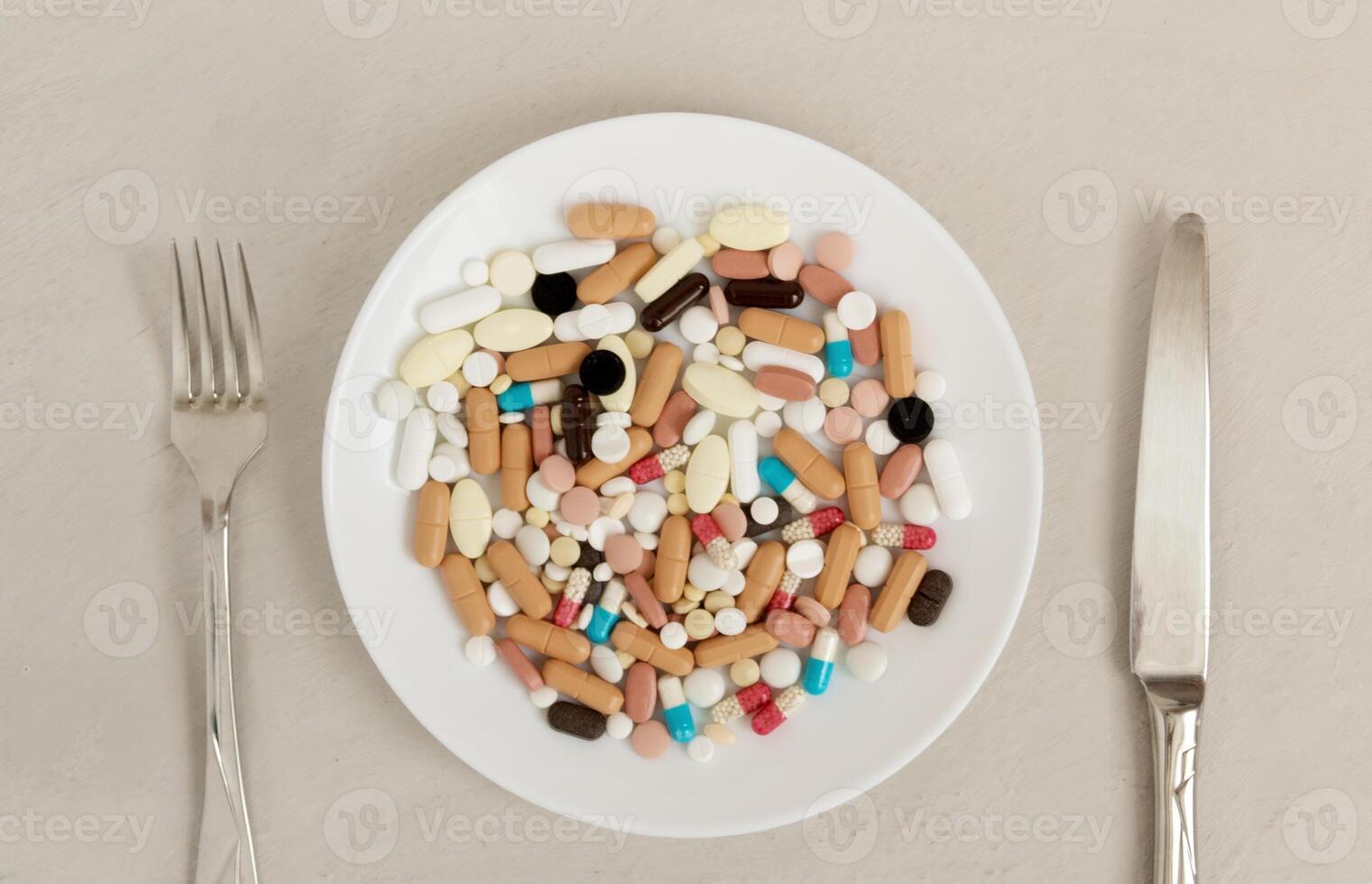 Plate of pills fork and knife next to it. Concept of excessive consumption of drugs that replace healthy diet. photo