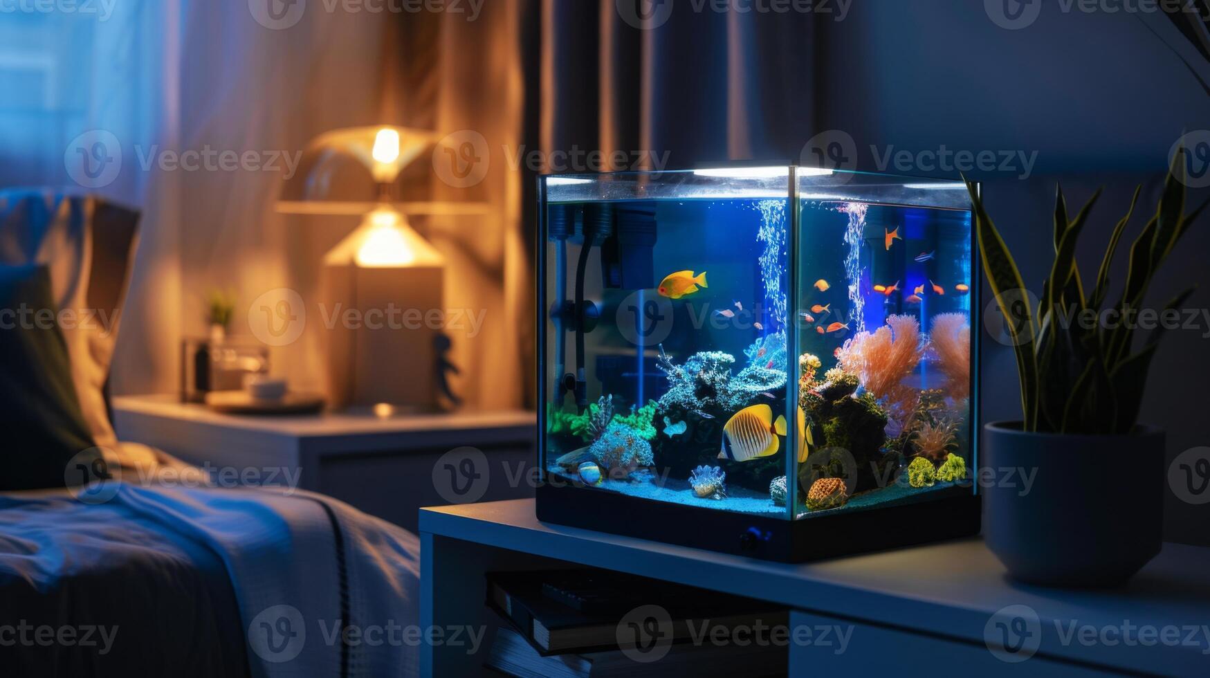 A small, square fish tank sits on a nightstand next to a bed, illuminated by a lamp in the background. The tank is filled with colorful fish and plants. photo
