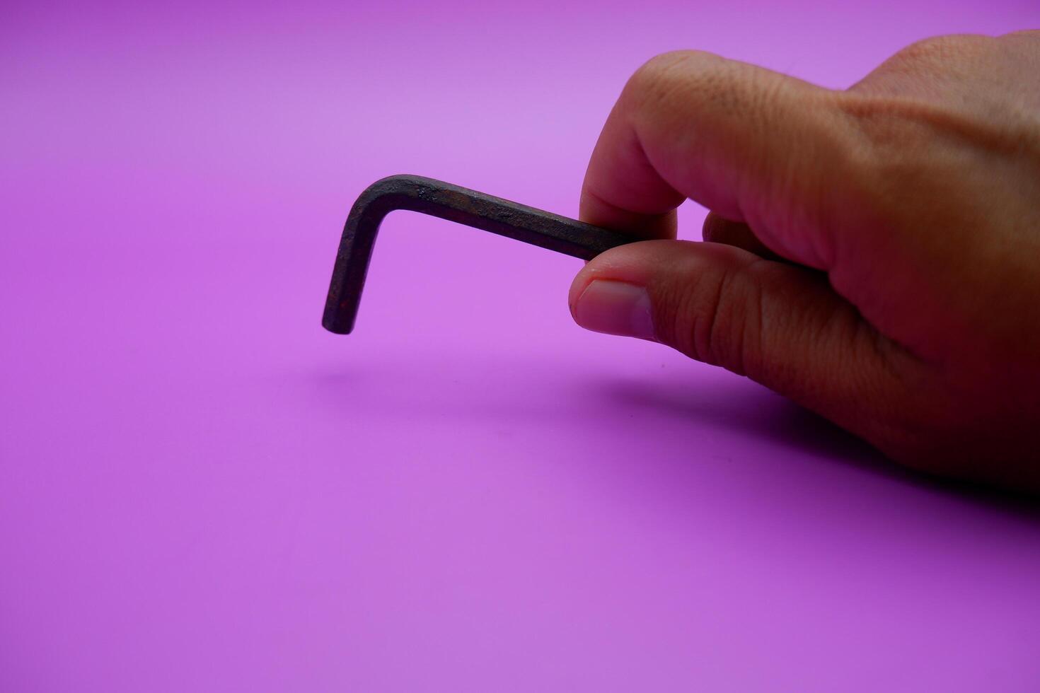 hand holding an L key. Allen key isolated on purple background photo
