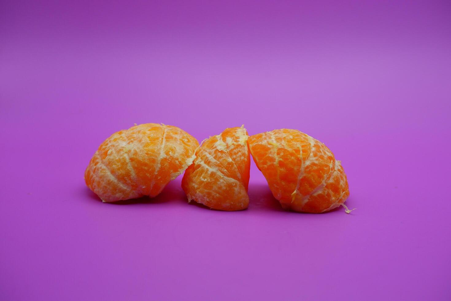 oranges that have been peeled and divided into several parts. orange isolated on purple background photo