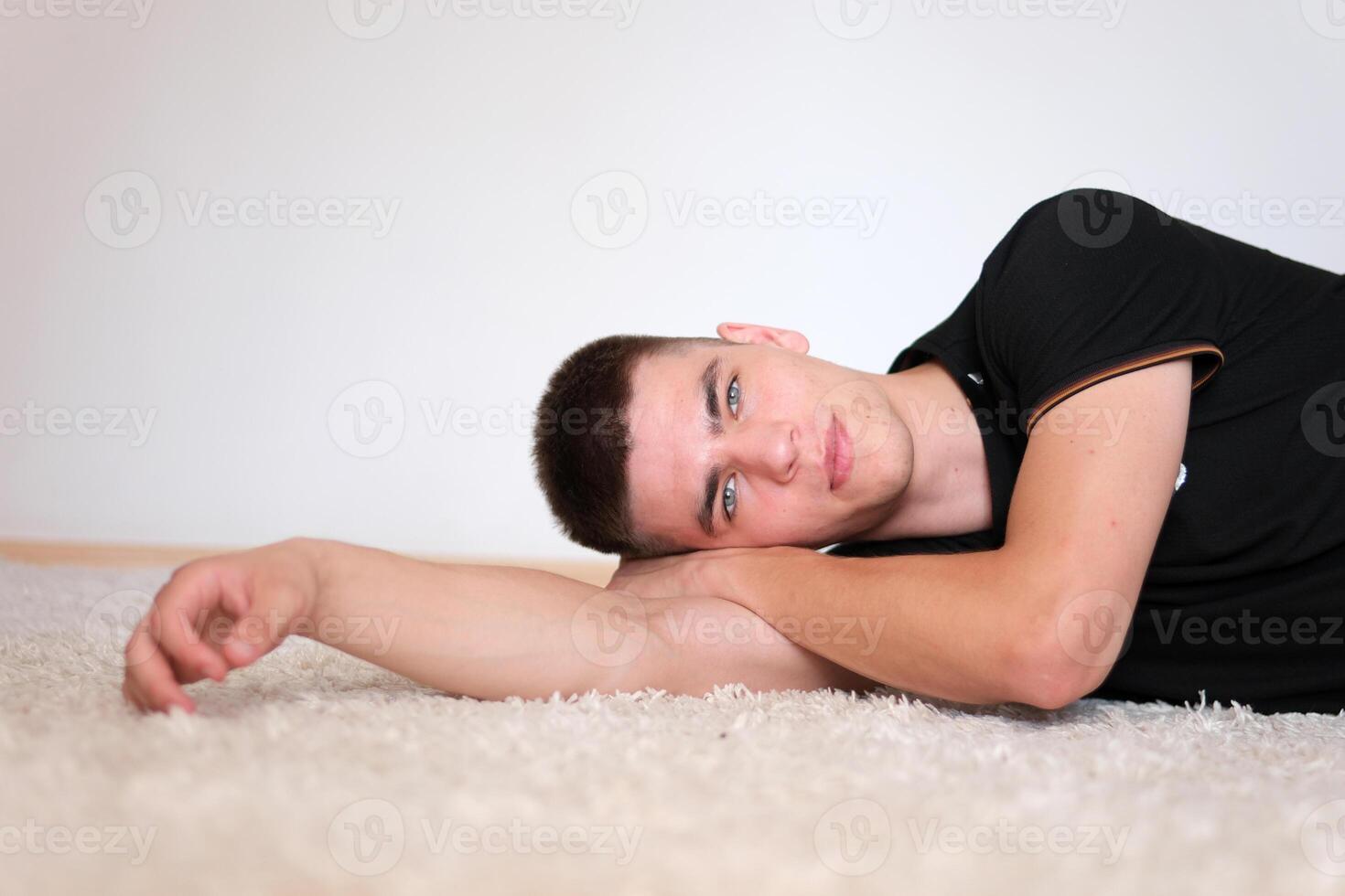 Sexy guy lying down put head on his hand lying on a white carpet resting relaxation. Handsome man with black hair and blue eyes. Mixed race nationality. photo