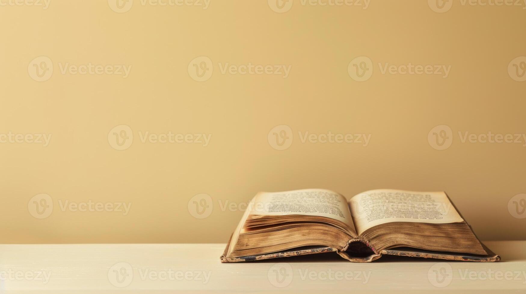 An open book lies on a white surface, with a tan wall behind it photo