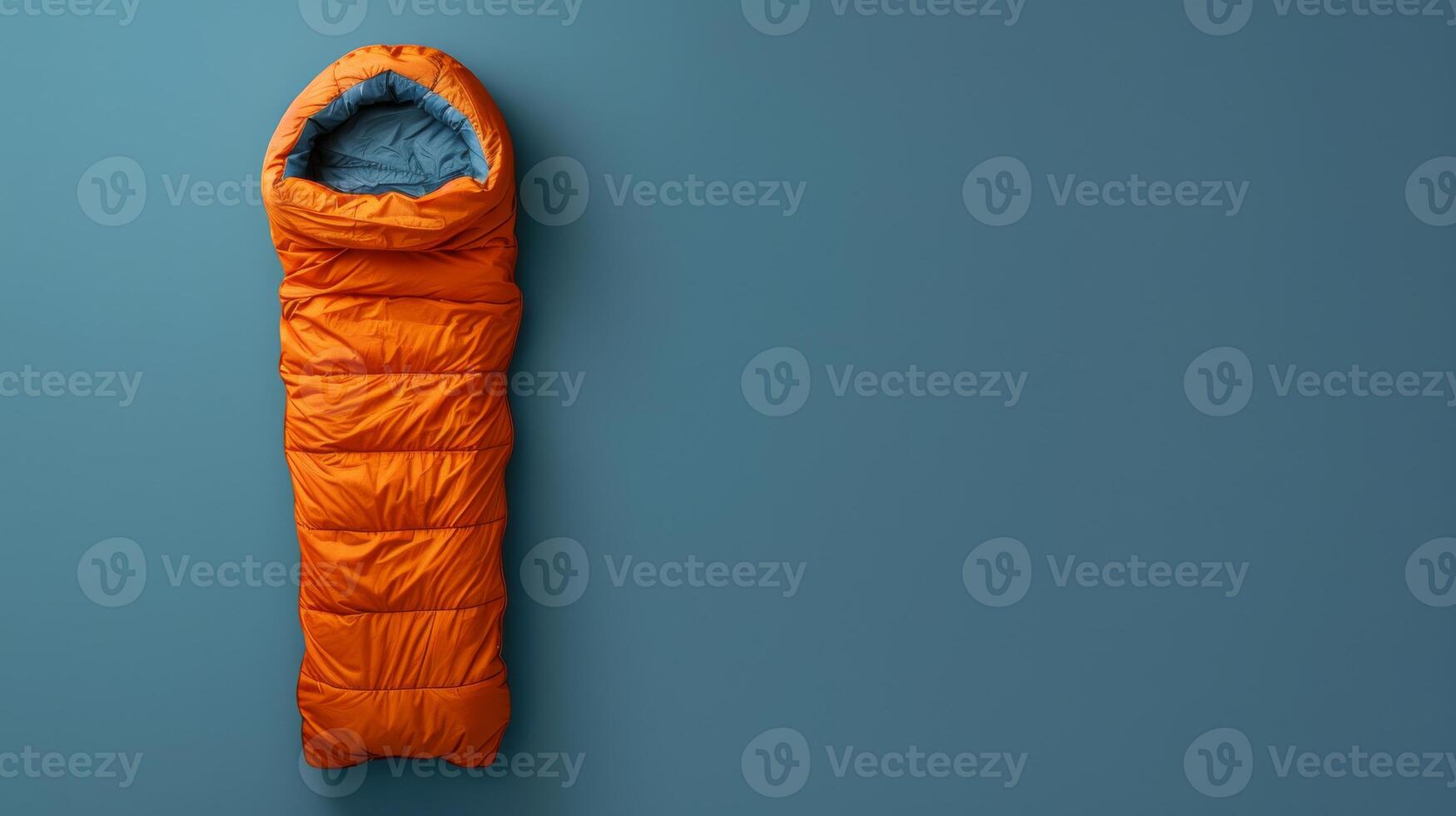 A bright orange sleeping bag rests against a blue background photo