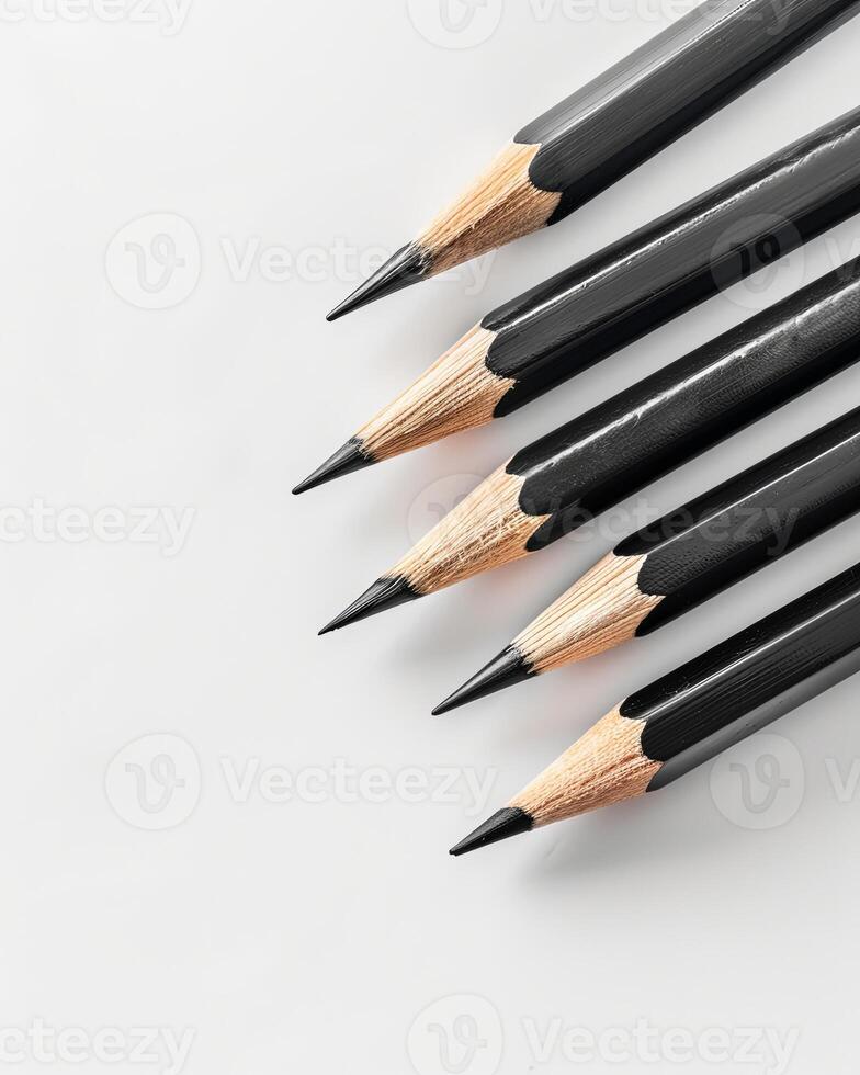 Five black pencils lie on a white surface, ready for drawing or writing photo