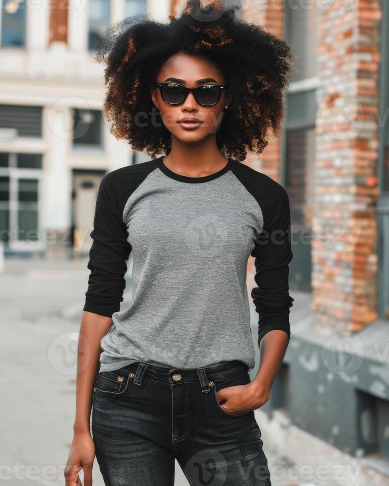 A stylish woman in a gray raglan shirt stands confidently against a brick wall photo