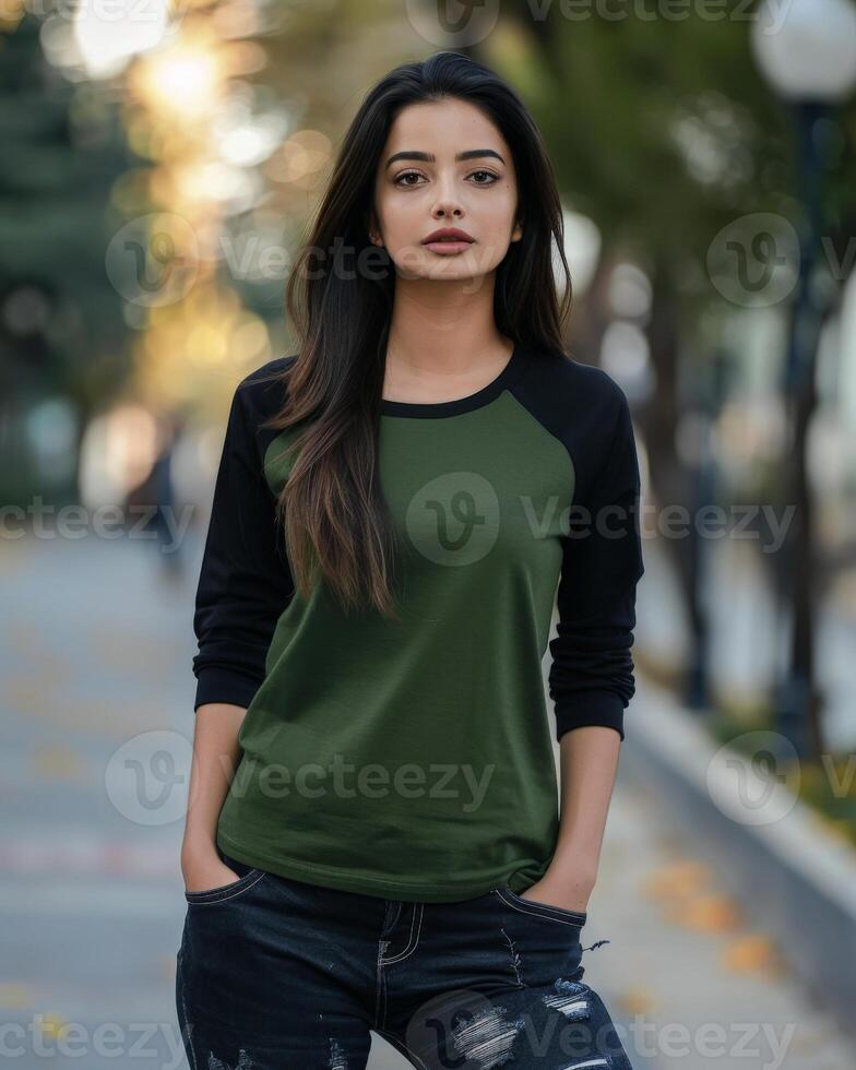 A woman wearing a green and black raglan shirt stands in an urban setting photo