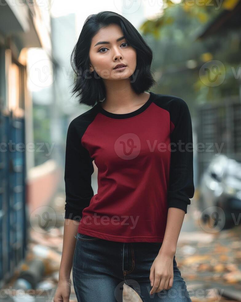A young woman wearing a red and black raglan shirt stands on a city street photo