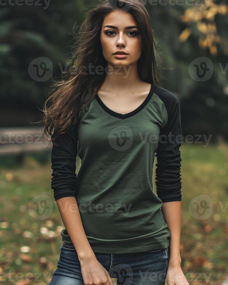 A woman in a green raglan shirt stands in a forest, posing for the camera photo