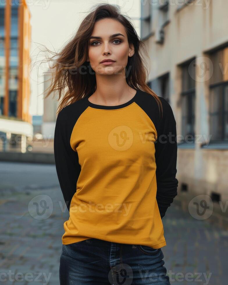 A young woman wearing a yellow raglan t-shirt with black sleeves stands on a city street photo